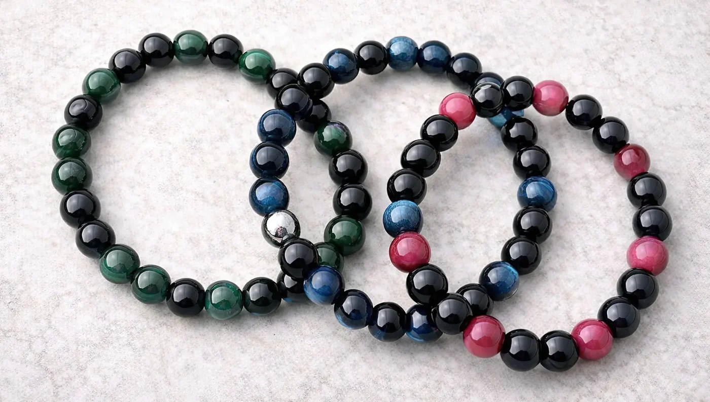 Bracelets en perles naturelles noires avec pierres vertes, bleues et roses, vue de dessus sur fond clair