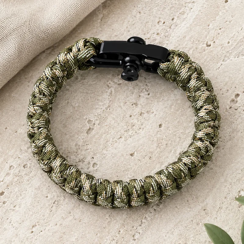 Bracelet de survie en paracorde camouflage présenté à plat sur fond de pierre claire