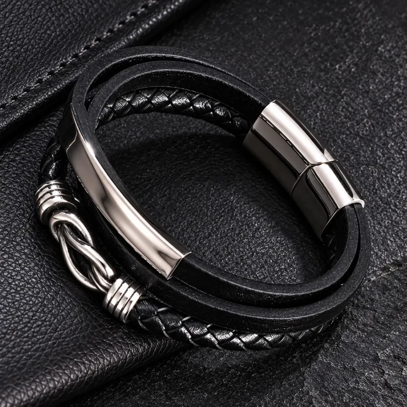 Bracelet homme en cuir noir multi-rangs avec signe infini argenté, présenté sur un fond en cuir noir.