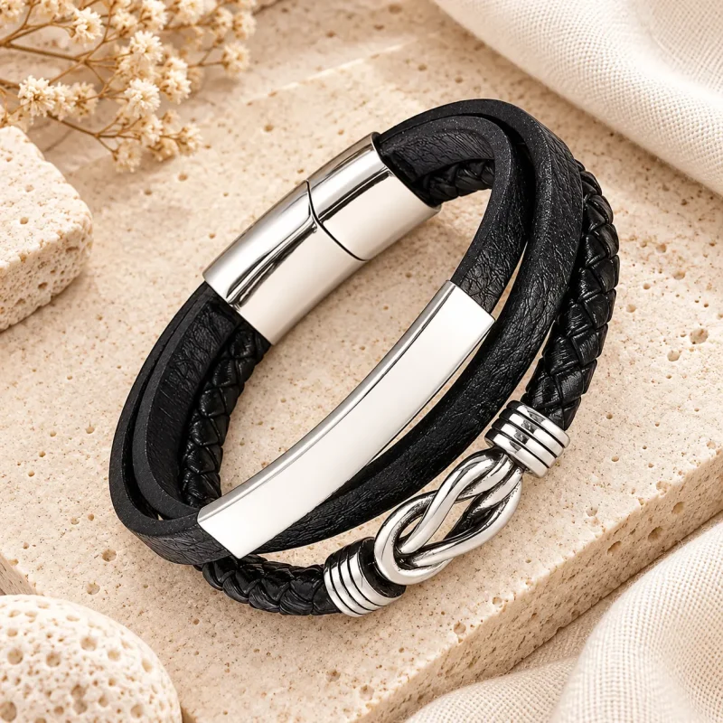 Bracelet infini homme en cuir noir multi-rangs avec motif argenté, présenté sur une pierre de travertin beige.